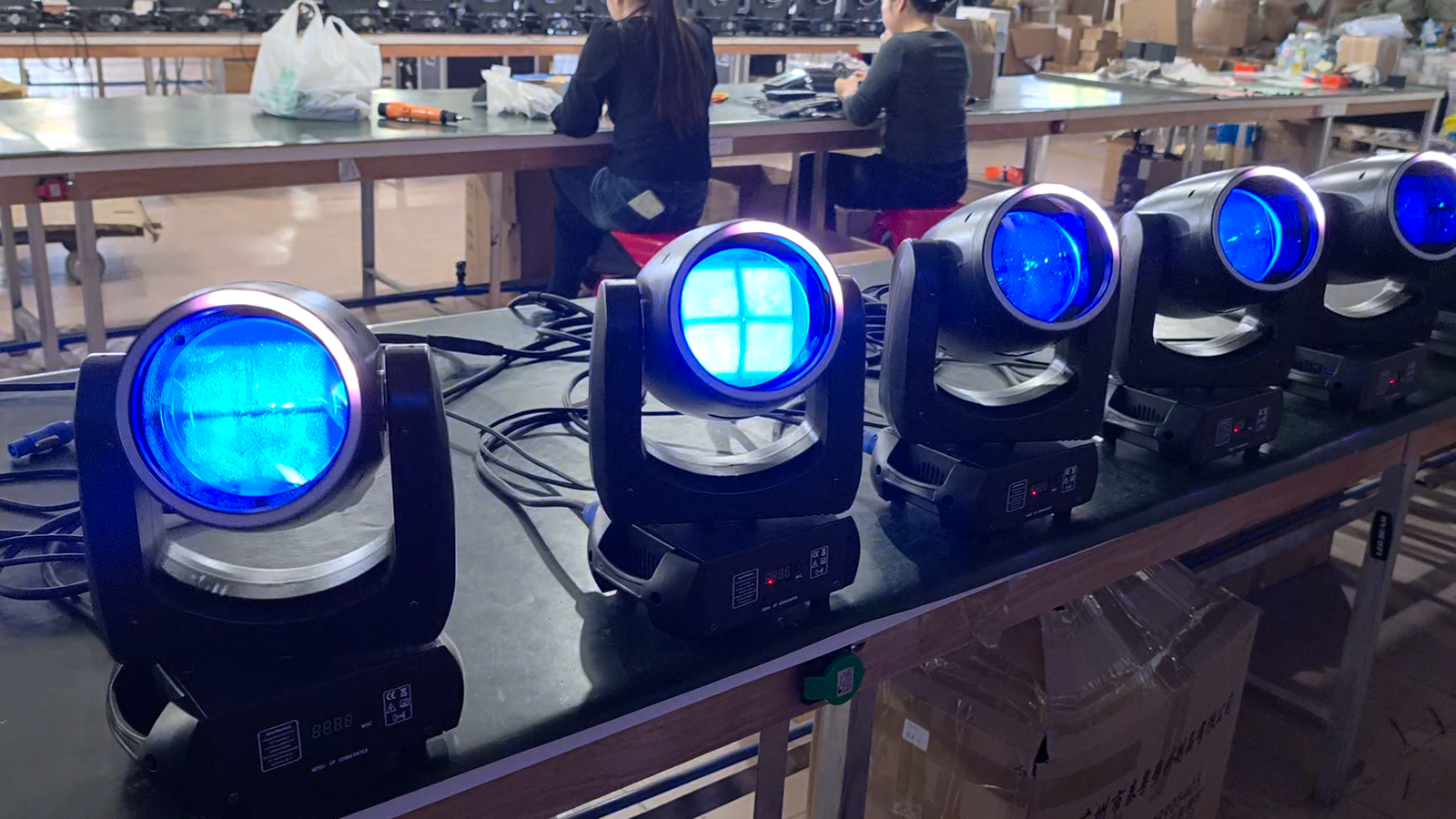 Row of beam moving heads powered on with blue lenses at a workshop bench