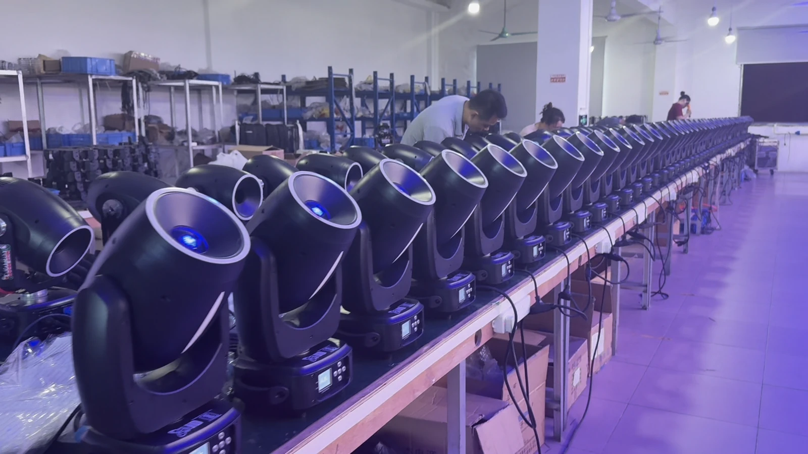 Rows of moving heads powered on at a workshop bench, viewed from the front
